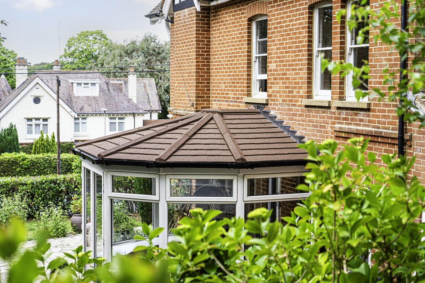 Victorian conservatory with brown tiles beside a mature garden